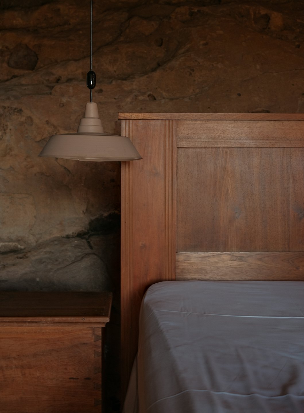 Letto in legno con lenzuola grigie appoggiato a una parete di pietra.