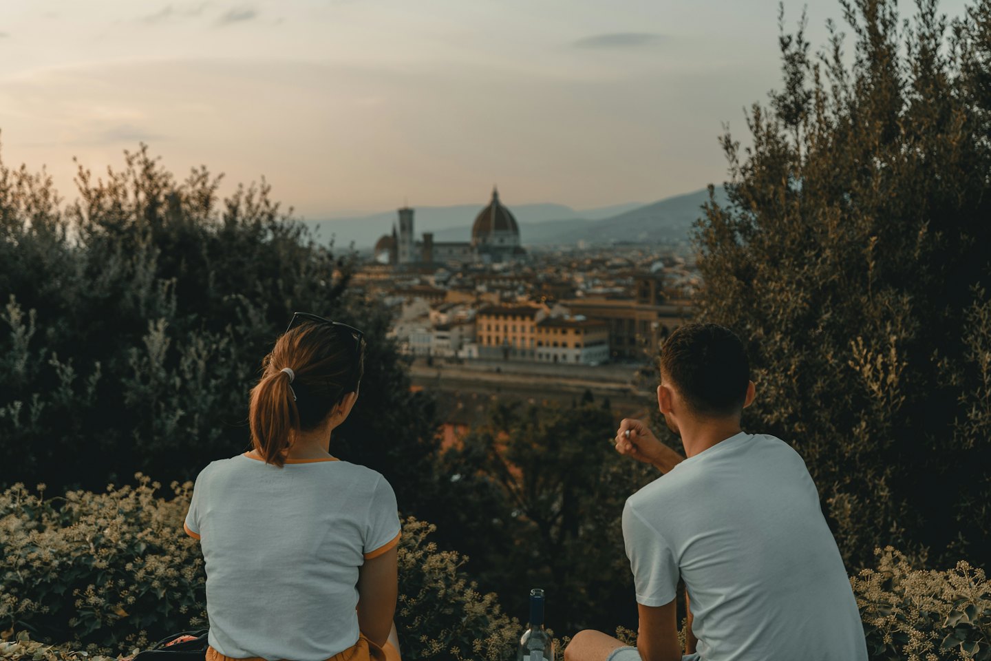 Coppia seduta su una collina al tramonto con vista su una città europea.